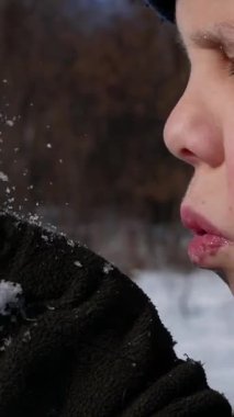 Güneşli bir kış gününde bir çocuk ellerinden neşeyle kar üflüyor. Kış eğlencesi, Noel havası.