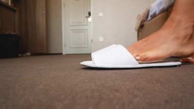 Kadınların ayakları yatak odasında beyaz terlikleri giyip öne doğru yürür. Ev ayakkabısı. Otel odası ayakkabıları..