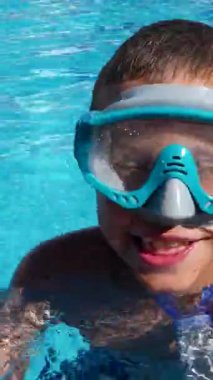 Maskeli ve şnorkeli olan sevimli bir çocuk havuzda yüzüyor ve havuz başında duruyor. Yaz tatili, çocuklarla aile tatilleri..