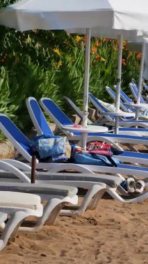 Taraf, Türkiye - 17 Haziran 2023: Akdeniz yakınlarındaki kumlu bir sahilde beyaz şemsiyeli güneş panzeleri sıraları. Yaz tatili ve turizm.
