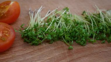 Freshly picked microgreens on a wooden kitchen board placed next to sliced tomatoes, panoramic view. Concept of healthy diet, vegan nutrition and organic lifestyle. Perfect for illustrating superfoods