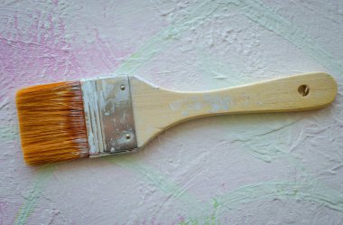 Düz bir boya fırçasının açık renkli desenli bir yüzeye uzanmış yakın plan fotoğrafı. Fırça, kıllarda ve kulpta sanatsal ve yaratıcı bir atmosfer yaratarak kullanım izleri gösteriyor.