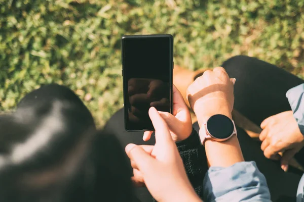 view of hand touching smart phone and smart watch screen, three people sharing social media information on smart mobile devices, natural green background out of focus