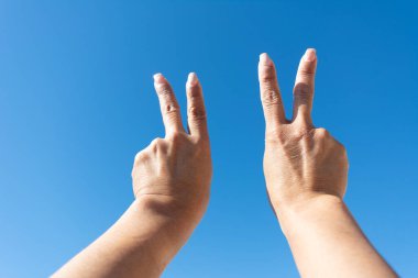 womans hands showing sign of victotia against blue sky background,