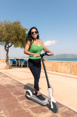 Elektrikli scooter kullanan bir kadın, tatil için tropik ada plaj beldesinde mutlu ve yaz gezisi. Şehir, sokak ve çevre dostu ulaşım, Escooter 'da eğlence Mallorca' da, Balear Adası 'nda ,