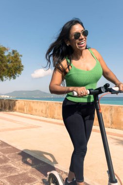 Elektrikli scooter kullanan bir kadın, tatil için tropik ada plaj beldesinde mutlu ve yaz gezisi. Şehir, sokak ve çevre dostu ulaşım, Escooter 'da eğlence Mallorca' da, Balear Adası 'nda,