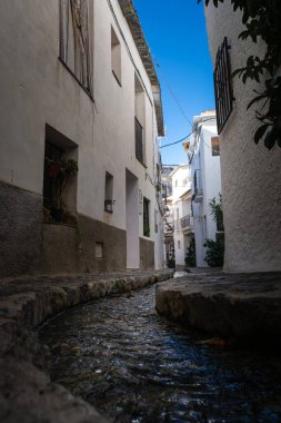 Parlak mavi gökyüzü altındaki dar beyaz binalardan akan küçük bir dere, Alpujarras, granada, Endülüs, Espa,