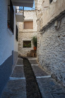 Parlak mavi gökyüzü altındaki dar beyaz binalardan akan küçük bir dere, Alpujarras, granada, Endülüs, Espa,