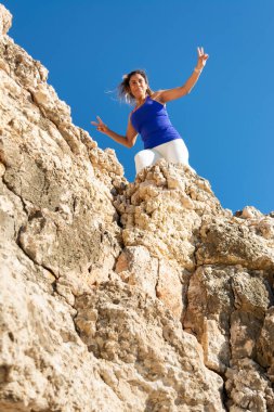 Kolları zaferle yükselen kayaların tepesinde duran kadın, Latin kadın, orta yaşlı, açık havada, Mallorca 'da psikobloğa tırmanan, balkulak adaları, İspanya,