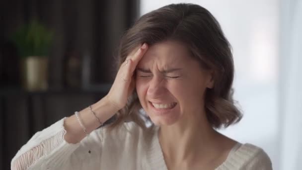 一个年轻的女人痛苦地扭头 双手抱头 在家里患有偏头痛 一个成年人的严重头痛发作 这种疾病的症状 脑血管痉挛 — 图库视频影像