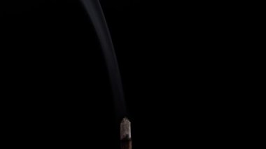 Clouds of fragrant smoke from a smoldering stick of incense for meditation, yoga and relaxation on a black background