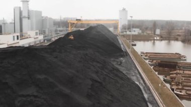 Sürüngen bir buldozer, ısıtma mevsiminde bir termik santralin fosil yakıt deposunda ısıtma konutları için kömür rezervlerini büyük bir yığına ayırıyor..