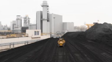 Sürüngen bir buldozer, ısıtma mevsiminde bir termik santralin fosil yakıt deposunda ısıtma konutları için kömür rezervlerini büyük bir yığına ayırıyor..