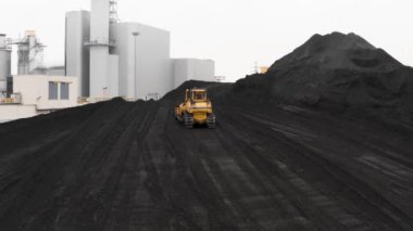 Sürüngen bir buldozer, ısıtma mevsiminde bir termik santralin fosil yakıt deposunda ısıtma konutları için kömür rezervlerini büyük bir yığına ayırıyor..