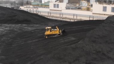 Sürüngen bir buldozer, ısıtma mevsiminde bir termik santralin fosil yakıt deposunda ısıtma konutları için kömür rezervlerini büyük bir yığına ayırıyor..