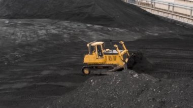 Sürüngen bir buldozer, ısıtma mevsiminde bir termik santralin fosil yakıt deposunda ısıtma konutları için kömür rezervlerini büyük bir yığına ayırıyor..