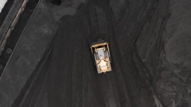 Sürüngen bir buldozer, ısıtma mevsiminde bir termik santralin fosil yakıt deposunda ısıtma konutları için kömür rezervlerini büyük bir yığına ayırıyor..