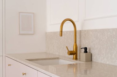 Mutfağın içinde altın gibi parlak bir musluk ve mermer tezgahın içine yerleştirilmiş dikdörtgen bir lavabo var. Kapatma vanalı karıştırıcı. Tesisat.