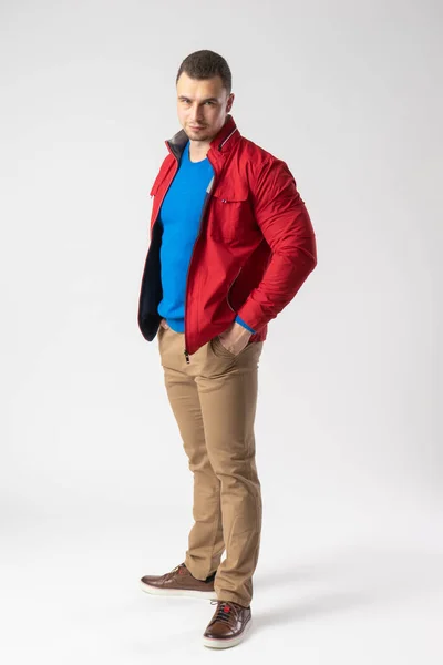 赤いジャケット 青いTシャツ ベージュのパンツを着た運動用の男が立ち ポケットに手を入れている 白地にポーズをとるモデル — ストック写真