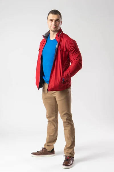 赤いジャケット 青いTシャツ ベージュのパンツを着た運動用の男が立ち ポケットに手を入れている 白地にポーズをとるモデル — ストック写真