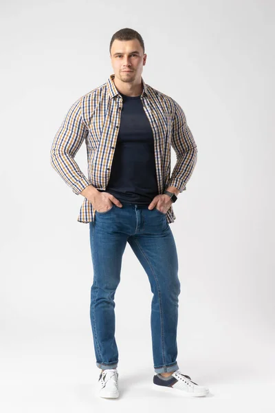 一个身穿格子呢休闲衫 蓝色T恤和牛仔裤的运动员站在他的臀部上 在白色背景上的模型 — 图库照片