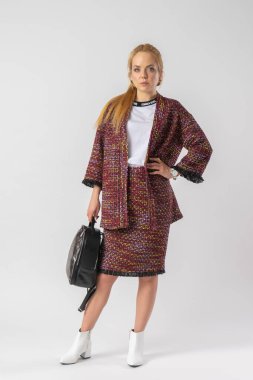 Sıradan, sıcak ofis kıyafeti giymiş, elinde bir çantayla genç bir sarışın. Stüdyoda beyaz arka planda poz veren bir model..