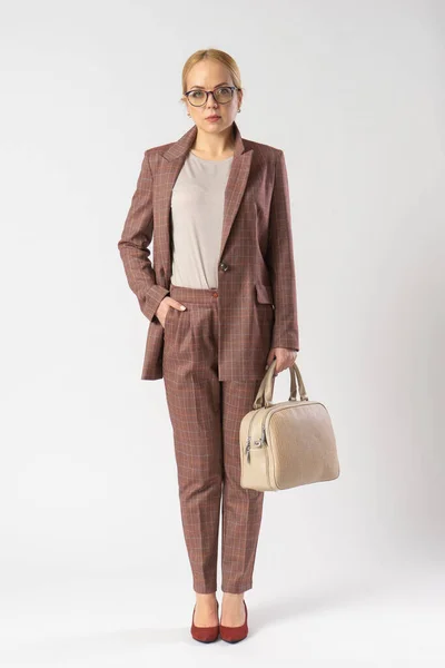 Gözlüklü genç sarışın bir kadın ve elinde bir kadın çantasıyla sıradan bir ofis elbisesi. Stüdyoda beyaz arka planda poz veren bir model..