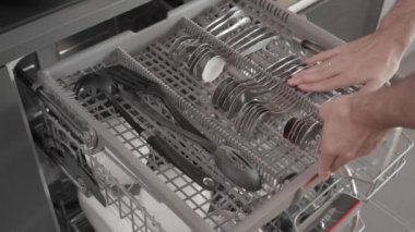 Bir adam kirli tabakları koyar, çatalları ve bardakları kirli bulaşık makinesine doldurur, ekolojik modu açar ve çamaşır makinesini çalıştırır. Mutfağı temizliyorum..