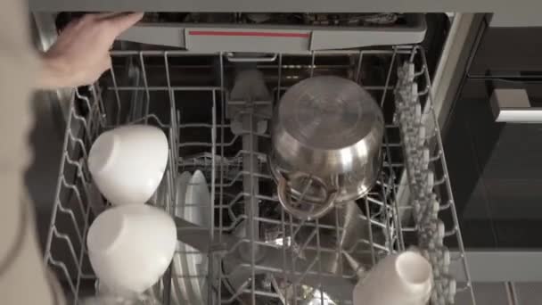这名男子把脏盘子 一个壶和一个煎锅放进一个装满脏盘子的家用洗碗机中 打开生态模式 开始洗涤循环 厨房里的清洁 — 图库视频影像