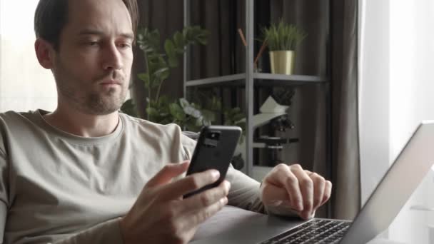 Man Carefully Looks Scrolls Contents Smartphone Screen Types Text Laptop — Stock Video