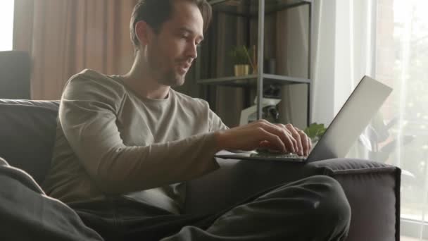 一个男人在家里的沙发上 用笔记本电脑通过视频链接进行了生动的交流 虚拟通信和远程协同工作 — 图库视频影像