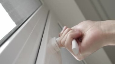 Bir adamın eli pencere çerçevesinin sapını çevirir ve odayı havalandırmak, temiz hava almak ve sıcaklığı ve nemi değiştirmek için PVC plastik penceresini hafifçe açar..