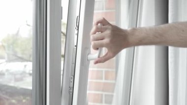 Odayı havalandırdıktan sonra, adam biraz aralık PVC plastik pencereyi eliyle kapatır ve pencereyi sıkıca kapatmak ve evi sıcak tutmak için kapı kolunu çevirir..