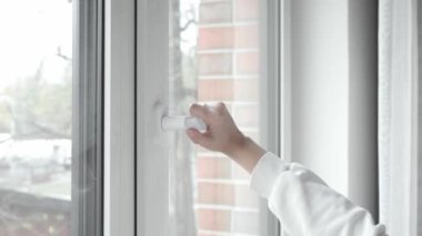 Bir kadının eli pencere çerçevesinin sapını çevirir ve bir PVC plastik pencere açar, temiz hava girmesini sağlar ve odadaki sıcaklık ve nemi değiştirir..