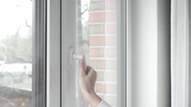 Kadın, plastik pencere çerçevesinin sapını eliyle çevirir ve odayı havalandırmak, temiz hava almak ve içerideki sıcaklığı değiştirmek için havalandırma modunda PVC penceresini açar..