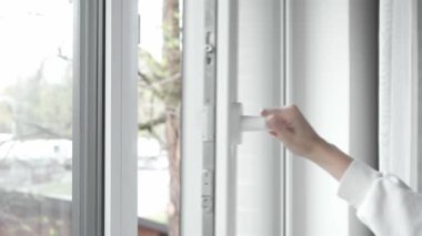 Bir kadının eli, odayı havalandırdıktan sonra, açık PVC plastik pencereyi kapatır ve pencere çerçevesini sıkıca kapatmak ve odayı sıcak tutmak için kilit mekanizmasının kolunu çevirir..