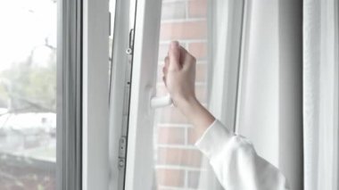 Odayı havalandırdıktan sonra kadın hafif aralık PVC plastik pencereyi eliyle kapatır ve pencereyi sıkıca kapatmak ve evin ısısını korumak için kolu çevirir..