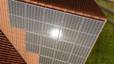 Özel bir evin kiremitli çatısına yerleştirilmiş fotovoltaik güneş hücrelerinde güneş parlaması. Elektrik faturalarını ödemenin maliyetini düşürmek için güneş enerjisiyle çalışan bir ev elektriği tedarik sistemi..