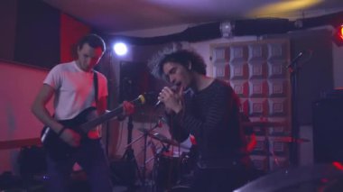 Bir müzik grubunun solisti mikrofona duygusal olarak şarkı söylüyor. Vokalist şarkının performansını elektro gitar ve bateri eşliğinde bando odasında prova eder..