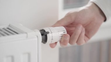 Adam radyatör termostatının vanasını çevirerek evin ısıtma gücünü maksimum değerden ekonomik moda düşürüyor ve pencereyi hafifçe açıp içeri temiz hava giriyor..