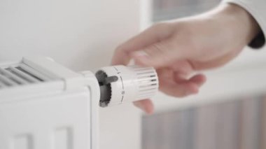 Adam radyatör termostatının değerini ortalama ekonomi modundan, evin ısıtmasını kapatmak için sıfıra eşit minimum değere ayarlar ve odayı soğutmak için pencereyi açar..