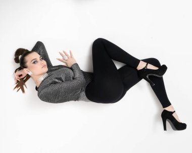 Makyajlı ve etkileyici mücevherleri olan çekici bir kız stüdyoda yerde yatıp kameraya bakıyor..