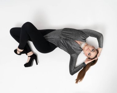 Parlak makyajlı, at kuyruklu ve etkileyici elmas takıları olan güzel bir kadın stüdyoda yere uzanmış kameraya bakıyor..