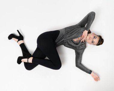 Makyajlı ve etkileyici mücevherleri olan çekici bir kız stüdyoda yerde yatıp kameraya bakıyor..