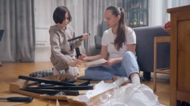 Anne ve oğlu yerde yatan parçalardan bir sandalye yapmak için birlikte zaman geçiriyorlar. Ebeveyn, mobilyaların kendiliğinden montajı talimatlarına uygun olarak çocuğa detayları verir..