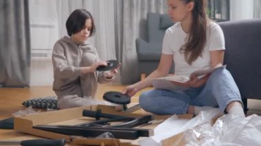 Bir anne çocuğuna eğlenceli bir şekilde yararlı beceriler öğretir, mobilyaları kendi kendine montaj talimatlarına uygun şekilde monte ederek, odada yerde oturarak. Ebeveynlik ve aile aktiviteleri