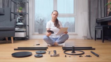 Parçaların önünde oturan bir kadın dikkatlice talimatlara bakar ve mobilyaları monte etmek için gerekli elementi seçer..