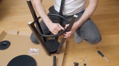 Adam cırcır tornavidayla vidaları sıkıca sıkıyor ve bir takım parçalardan yeni bir tabure yapıyor. Evdeki mobilyaların kendiliğinden montajı üzerine üreticisinden video eğitimi.