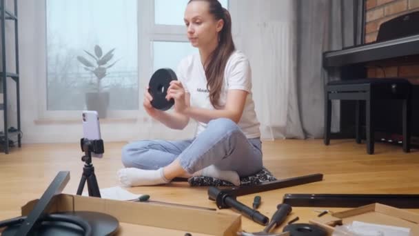 블로거 소녀는 그녀의 채널의 가입자를위한 삼각대에 카메라에 가구의 조립을위한 부품의 — 비디오