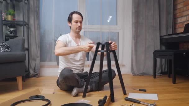 Człowiek Samodzielnie Montuje Nowe Krzesło Siedząc Podłodze Przed Narzędziami Ręcznymi — Wideo stockowe